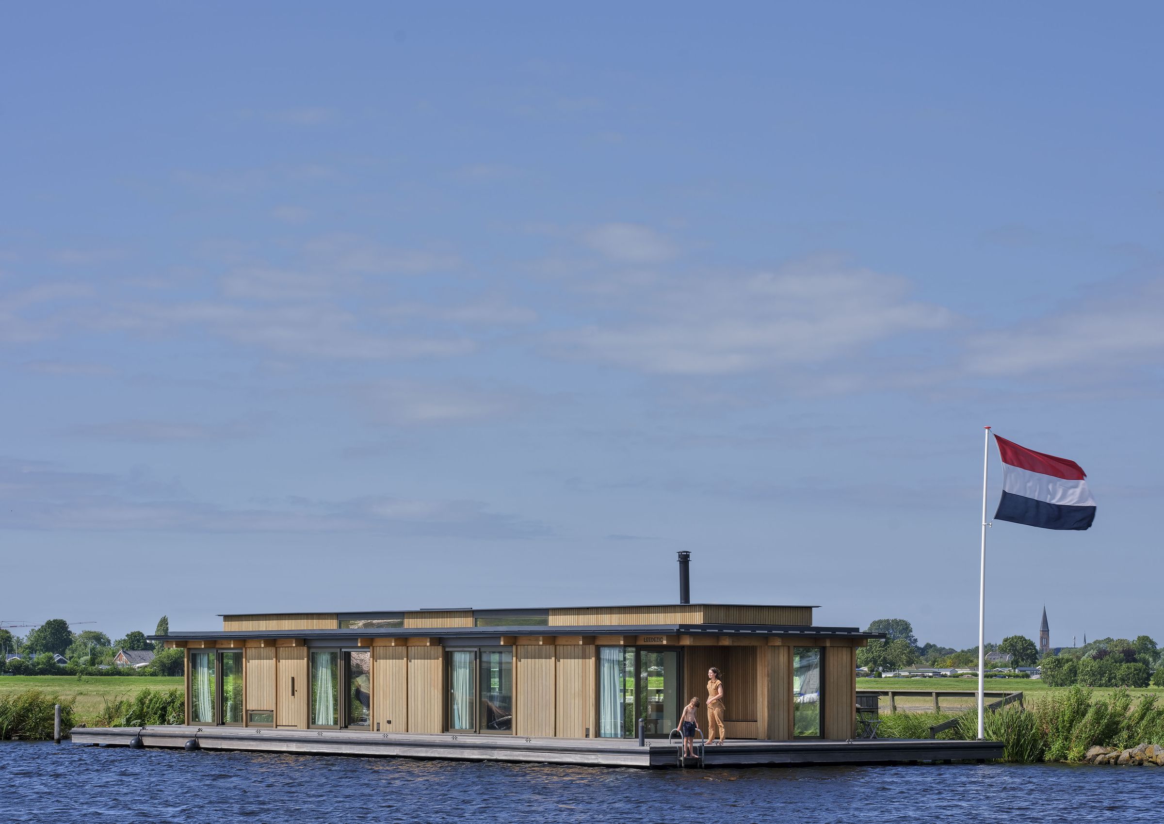 Drijvende woning in Warmond met eiken gevel, gezien over het water, met een Nederlandse vlag