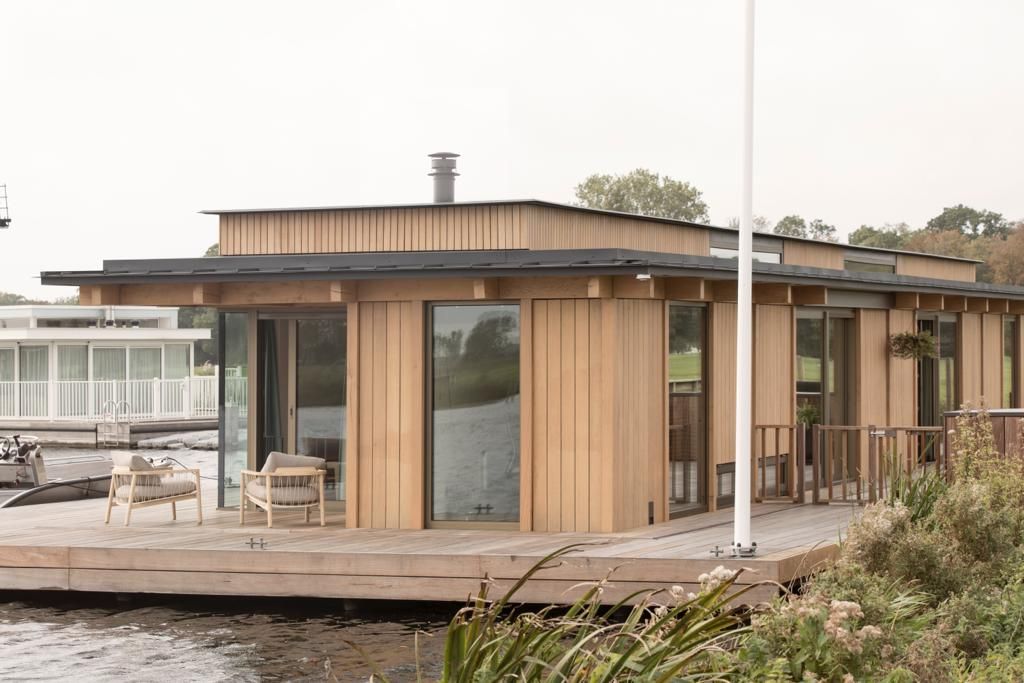 Drijvende woning met een ruim houten terras en tuinstoelen aan het water