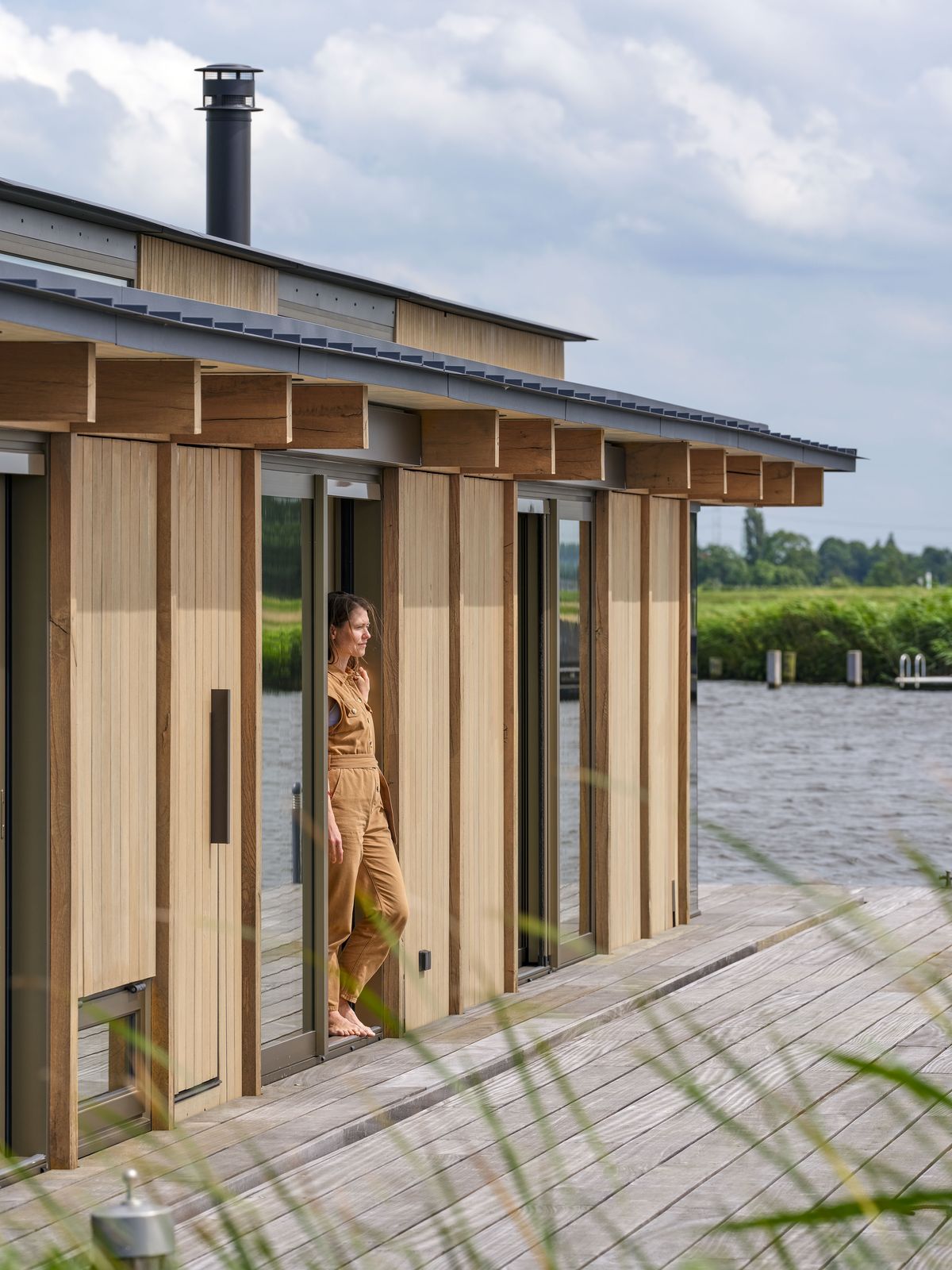 Vrouw in de open deur van de woning in Warmond, op het houten dek aan het water